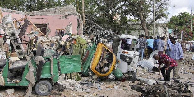 Passanten stehen in Mogadischu neben ausgebrannten Fahrzeugwracks