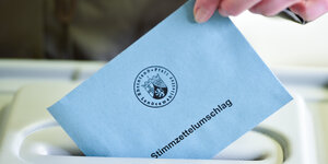 Eine Hand steckt einen Stimmzettel in einen Schlitz