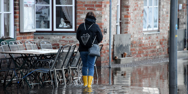 Frau mit Regenstiefeln vor einer Hausfassade im überschwemmten Lübeck