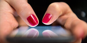 Die rot lackierten Daumen einer Frau tippen auf einem Smartphone