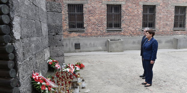 Beata Szydlo (r), und Kulturminister Piotr Glinski stehen vor einer Mauer, an die Blumenkränze gelehnt sind