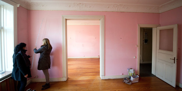 Zwei Frauen messen eine Zimmer mit rosafarbenen Wänden aus