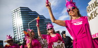 Frauen in pinkfarbenen Kleidern halten pinkfarbene Fackelattrappen in der Hand