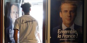 Ein Mann geht neben einem Plakat von Macron durch eine Tür ins Licht