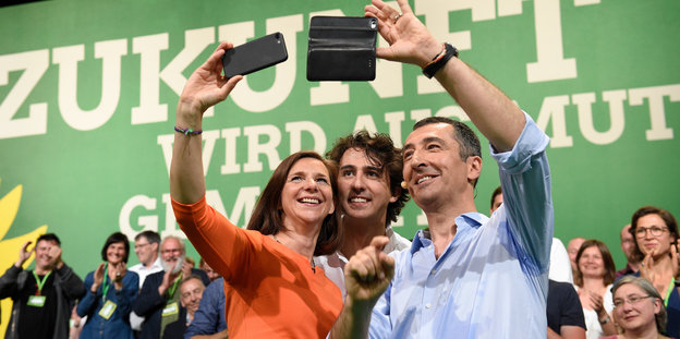 Drei Menschen machen ein Selfie vor der Kulisse des Grünen-Parteitags