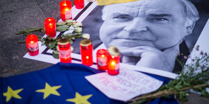 Eine Schwarzweiß-Aufnahme Helmut Kohls zwischen Kerzen, Blumen und einer Europaflagge