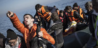 Flüchtlinge stehen auf einem kaputten Gummiboot, das auf der griechischen Mittelmeerinsel Lesbos angekommen ist