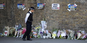 Eine Polizistin läuft an einer Wand entlang, an der viele Blumen lehnen
