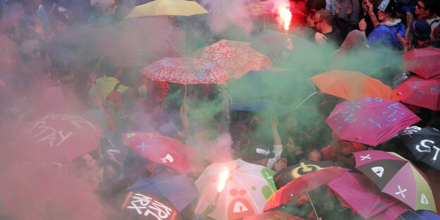 Bunte Rauchschwaden steigen über eine Menschenmenge unter bunten Schirmen empor