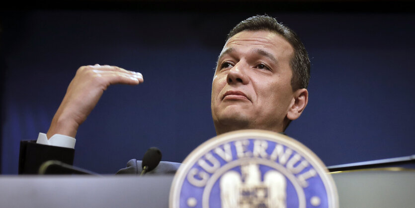 Ein Mann gestikuliert auf einem Podium mit der Hand