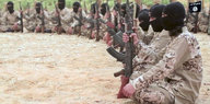 Kämpfer der Terrormiliz "Islamischer Staat" sitzen im Kreis, in der Hand halten sie Gewehre