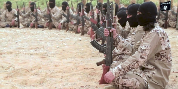 Kämpfer der Terrormiliz "Islamischer Staat" sitzen im Kreis, in der Hand halten sie Gewehre