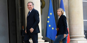 Ein Mann und eine Frau gehen eine Treppe hoch, im Hintergrund stehen eine EU- und eine Frankreich-Fahne