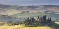 Blick auf eine hügelige Landschaft in Italien. Im Vordergrundein Wohnhaus zwischen Bäumen