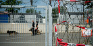 Polizist_innen mit Hunden hinter einem Gitter, das von Stacheldraht gesaäumt ist