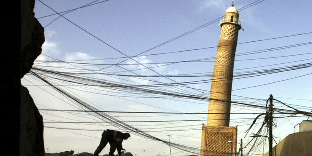 Stromleitungen und ein Mann vor dem schiefen Minarett im Hintergrund