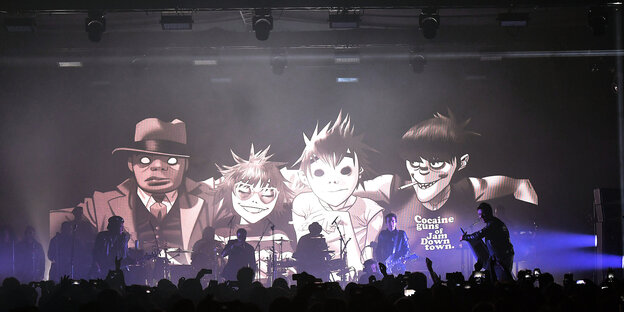 Musiker stehen auf der Bühne. Auf einer Leinwand hinter ihnen sind vier Comicfiguren zu sehen