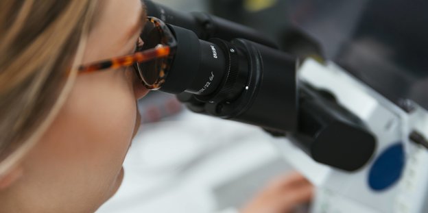 eine Frau mit Brille schaut durch ein Mikroskop