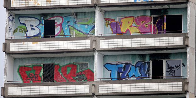 An einer Plattenbauwand zwischen Balkonen sind bunte Grafittis zu sehen