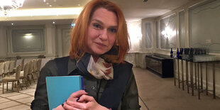 Asli Erdogan schaut lächelnd in die Kamera und hält eine blaue Mappe im Arm