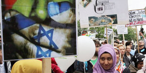 Demonstrantentragen ein Schild, auf dem eine Hand in den Farben der Flagge Israels einem Gesicht in den Farben der Flagge Palästinas den Mund zuhält