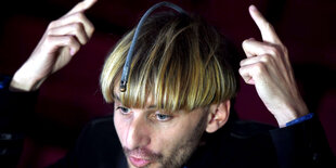 Der Cyborg Neil Harbisson zeigt auf eine Art Antenne auf seinem Kopf, mit der er Farben hören kann