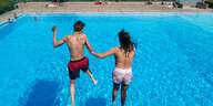 Ein Junge und ein Mädchen springen in einem Freibad von einem Sprungturm ins Wasser