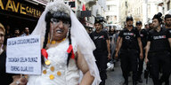 ein LGBTI-Community-Mitglied im Hochzeitskleid und mit Protestschild vor einer Reihe von Polizisten
