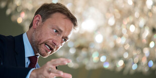 Christian Lindner steht unter einem glamurös glitzernden Kronleuchter und gestikuliert mit strenger Mine