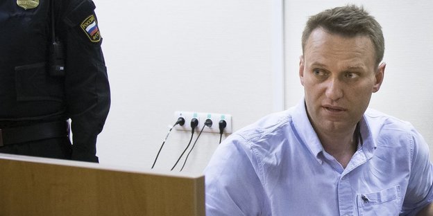 Nawalny sitzt im hellblauen Hemd am Rand des Bildes und guckt geknickt