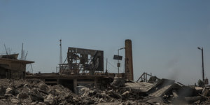 Die Überreste eines Posters der Terrormiliz Islamischer Staat hängen über Trümmerhaufen