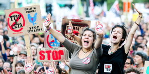 Zwei Frauen rufen und heben die Arme, hinter ihnen eine Menschenmenge. Schilder gegen Ceta und TTIP werden in die Höhe gehalten