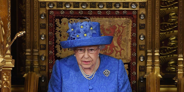 Eine ältere Frau mit großem blauen Hut und blauem Outfit