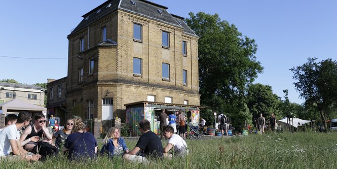 Menschen sitzen im Gras vor einem Gebäude