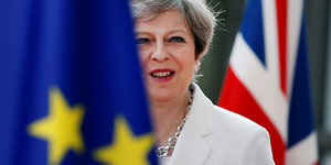 Theresa May steht zwischen einer Flagge der Europäischen Union und einer Flagge von Großbritannien