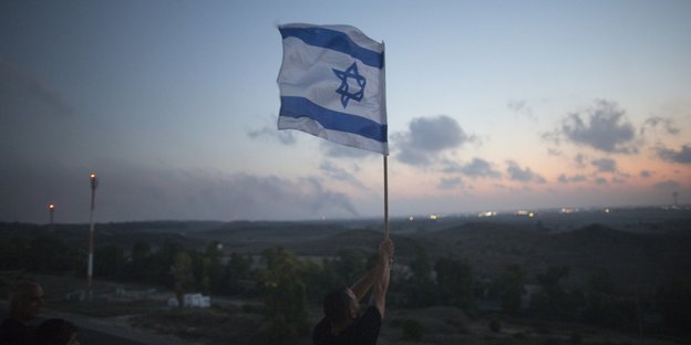 Ein Mensch hält eine Israelfahne in die Höhe