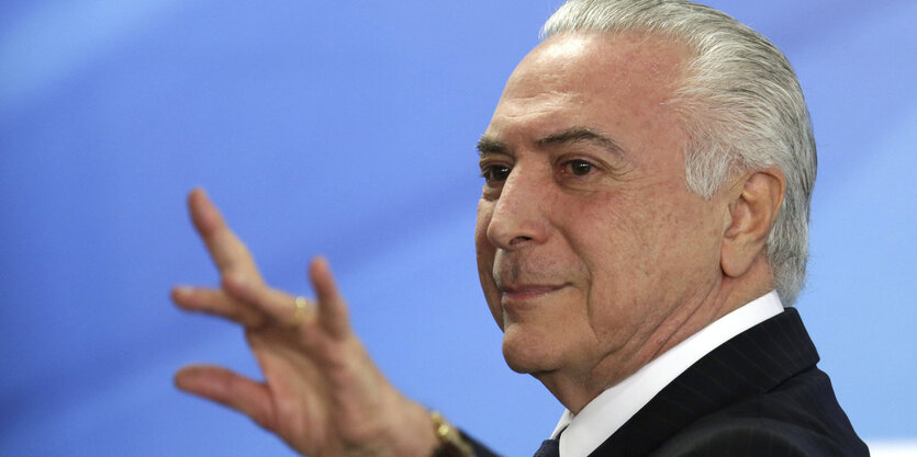 Präsident Temer hat das weiße Haar zurückgekämmt, guckt selbstgefällig und zeigt mit gespreizten Fingern nach vorne