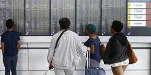 Menschen stehen vor einem Abflugplan am Flughafen