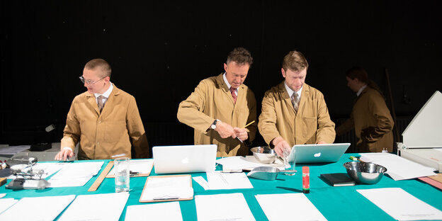 Drei Männer in braunen Laborkitteln hinter Tresen