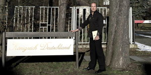 Peter Fitzek steht neben einem Schild mit der Aufschrift "Königreich Deutschland"