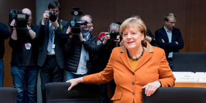 Angela Merkel lehnt an einem Stuhl, im Hintergrund Fotografen