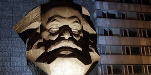 der angeleuchtete Kopf einer Karl-Marx-Statue vor einem Plattenbau