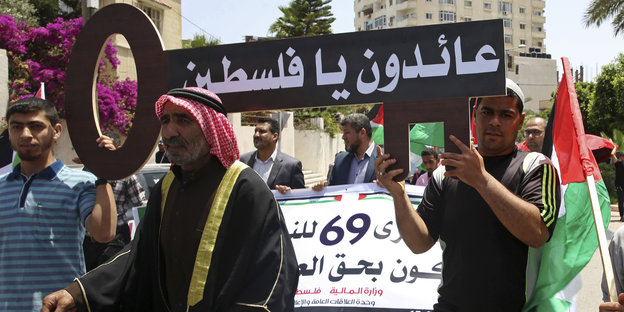 Palästinenser halten ein Schild hoch, in dem auf arabisch "wir kommen zurück Palästina" steht