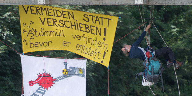 Ein Mann hängt an einem Seil neben einem Transparent mit der Aufschrift "Vermeiden statt verschieben"