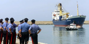 Polizisten stehen am Hafen, während ein Beibboot in Richtung Land fährt