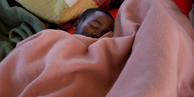Ein Junge schläft zwischen mehreren Bettdecken