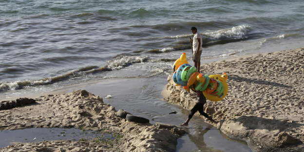 Ein Junge, der Schwimmutensilien verkauft, springt über einen Siel, der ins Meer führt
