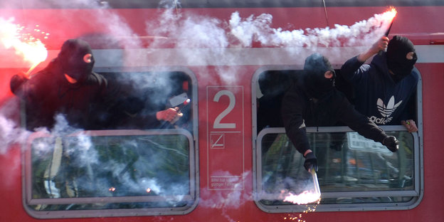 Vermummte Fußballfans halten Böller und Leuchtfackeln aus einem Zug