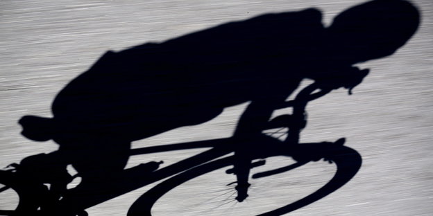 Man sieht den Schatten eines Radfahrers auf Asphalt