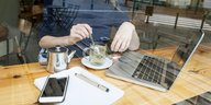 Eine Person arbeitet mit Laptop und Smartphone in einem Café